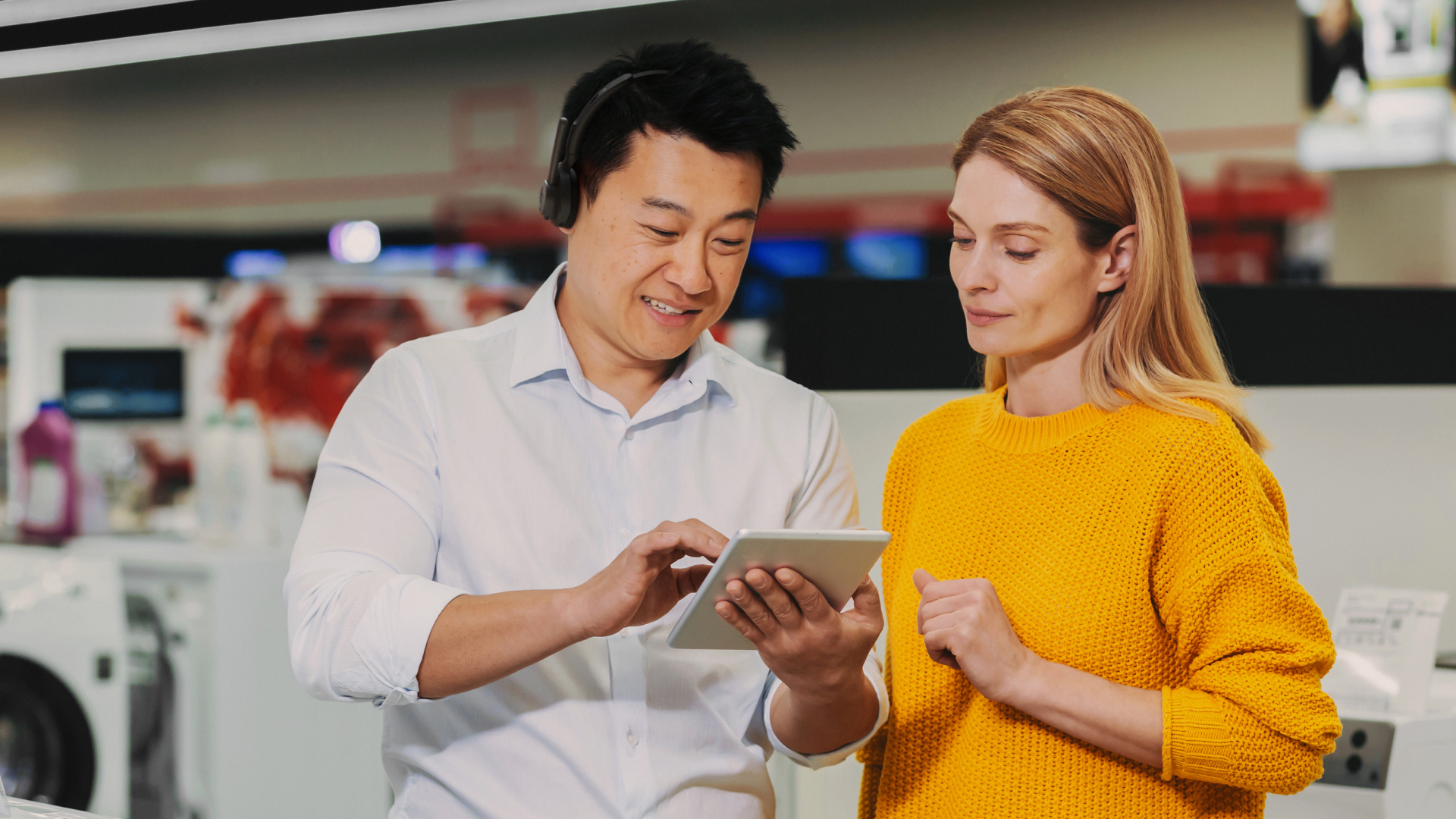 Retail employee wearing a Jabra Perform 55 headset shows a handheld device to a customer in a store.