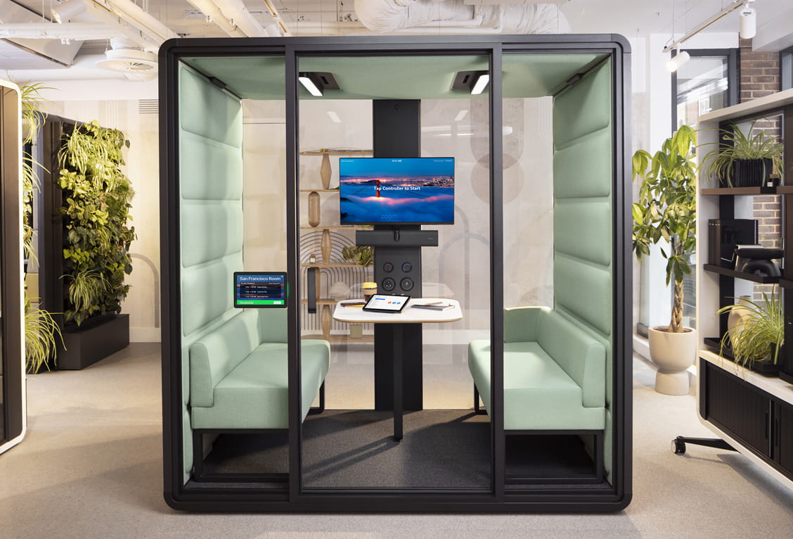 Jabra Scheduler tablet on glass of a modern meeting pod with mint‑green upholstered benches and wall display
